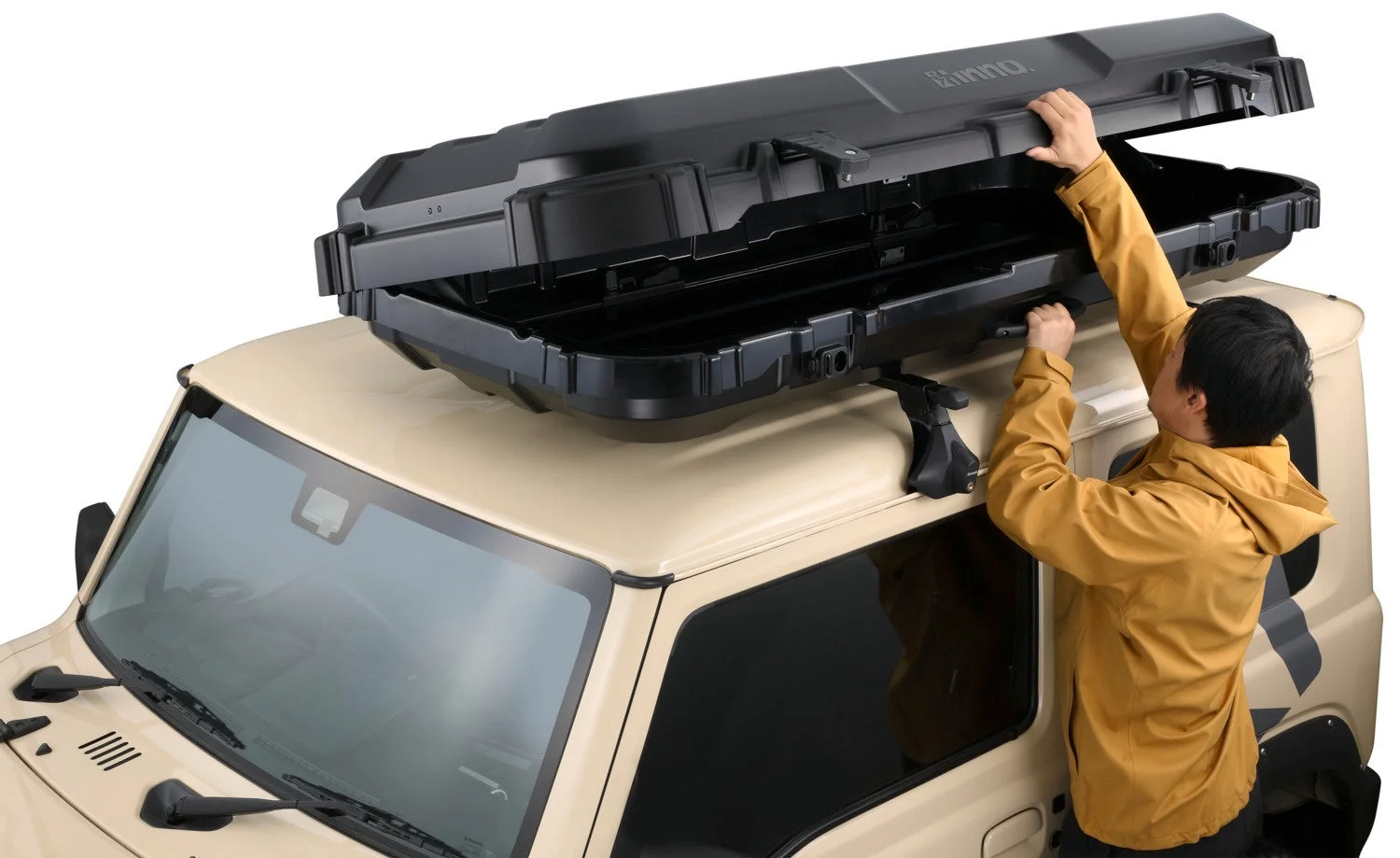 ベージュ色のオフロード車に装着された黒いルーフボックスを男性が開けている。キャンプやアウトドアレジャーでの荷物積載に役立つカー用品の利用シーン。