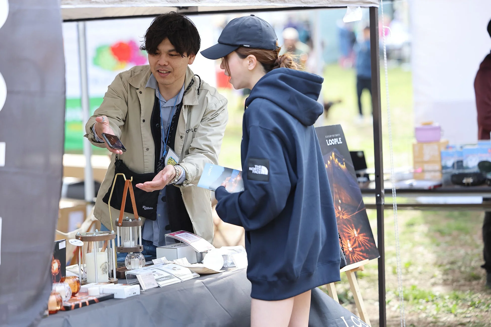 屋外イベントのブースで男性が商品について説明している様子