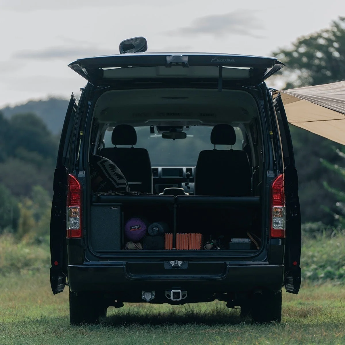 広大な自然の中で、バックドアを開けた黒いバンが写っています。