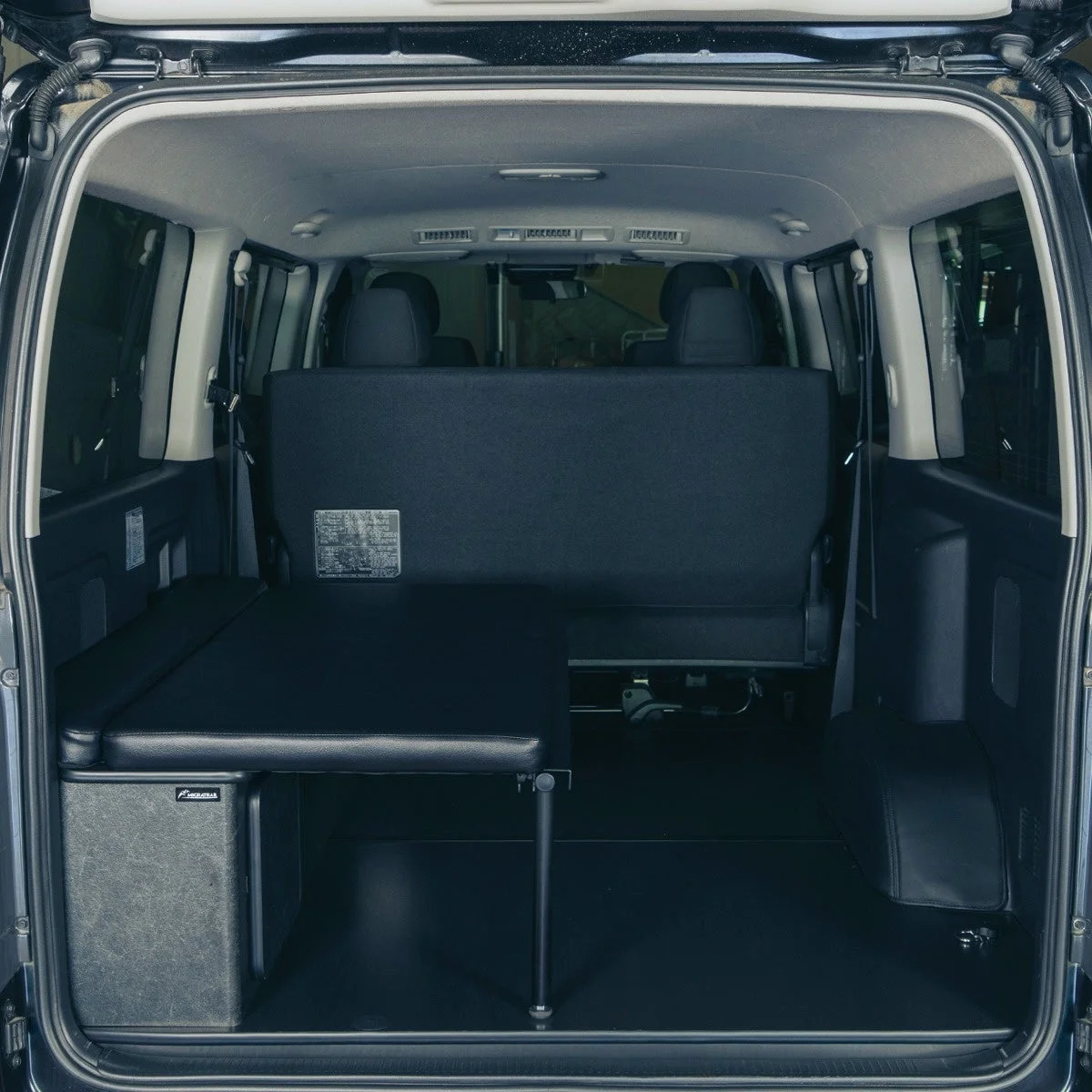黒いバンの後部座席と、荷室に設置された折りたたみ式のベッドまたはベンチが写っている。