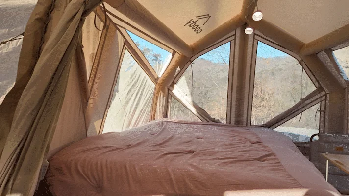 広々としたテントの内部で、快適そうなベッドが置かれ、窓からは自然豊かな山の景色が広がっている