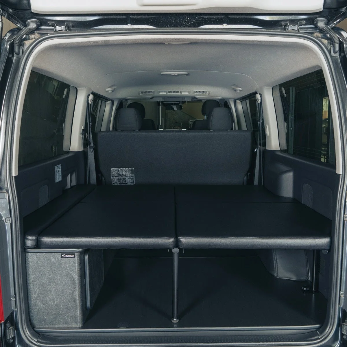 バンの後部座席から荷室にかけて、黒いベッドキットが設置されている車内の様子です。