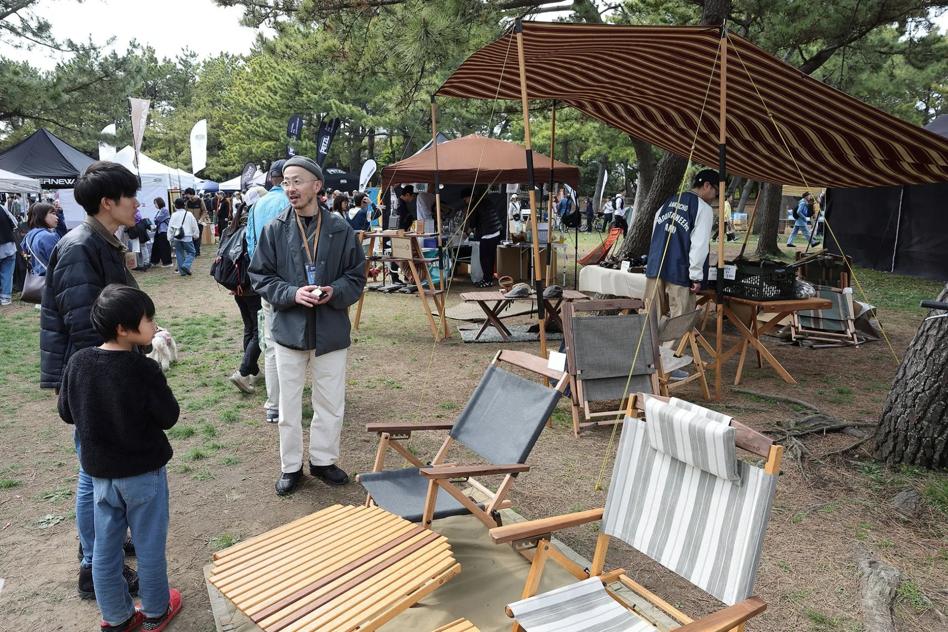 木々に囲まれた公園で開催されているアウトドアイベントで、家族連れが楽しんでいる様子