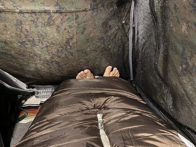 テントの中で寝袋に入った人の足が写っており、キャンプやアウトドアでの休息、リラックスしたひとときを感じさせる画像です。