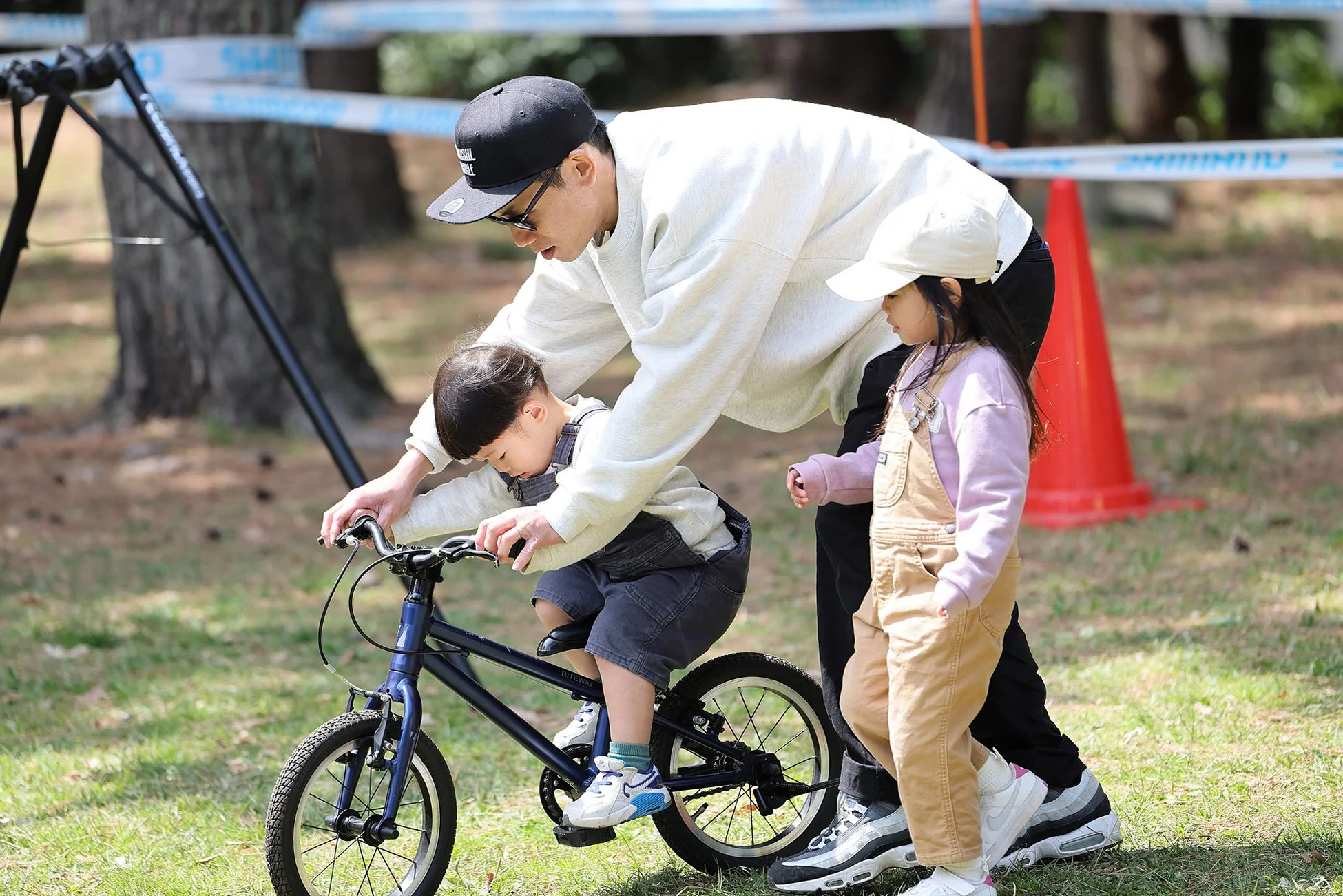 公園の芝生で父親が幼い息子に自転車の乗り方を教えている様子