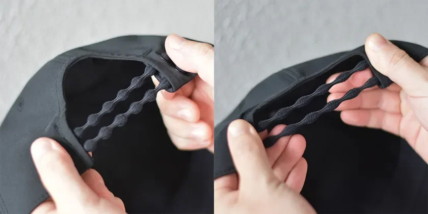 黒い帽子（またはキャップ）の内側にある波状のゴム製アジャスターを、両手で引っ張って調整している様子を捉えた画像です。フィット感を高めるための機能的なデザインが特徴です。