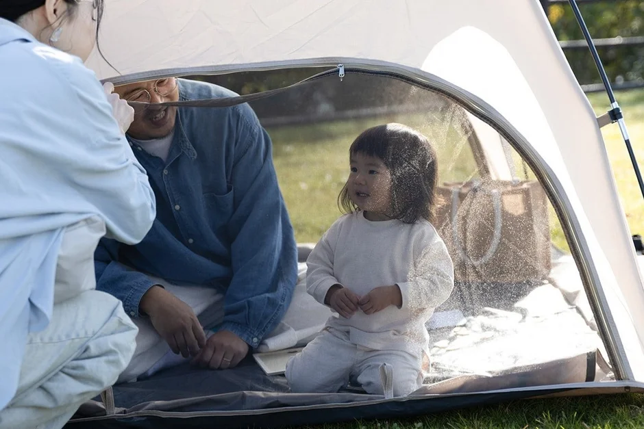 屋外でテントに入り、楽しそうに過ごす家族の様子