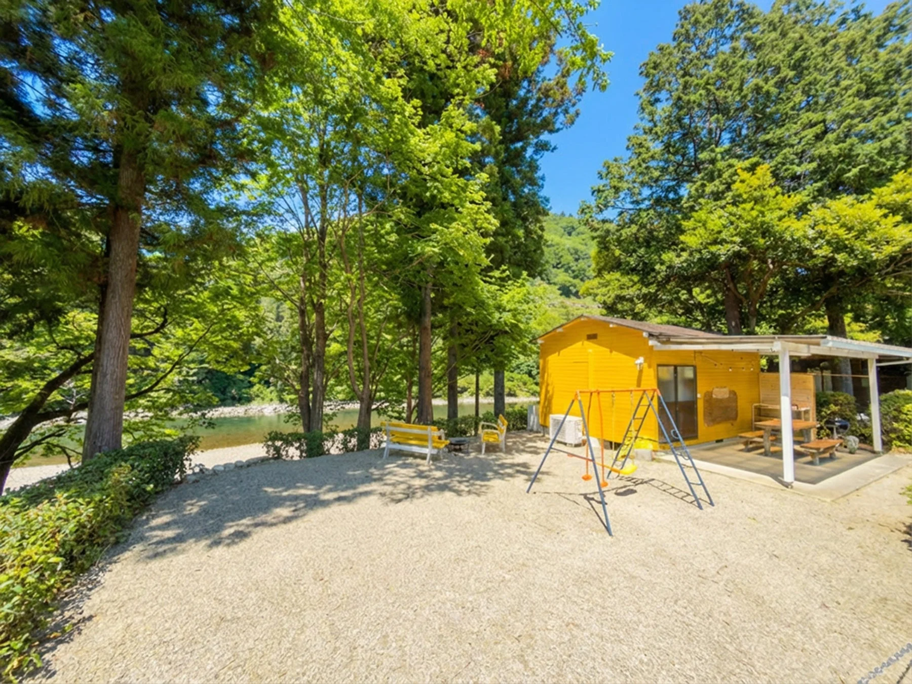 緑豊かな木々に囲まれた川沿いの黄色いコテージ