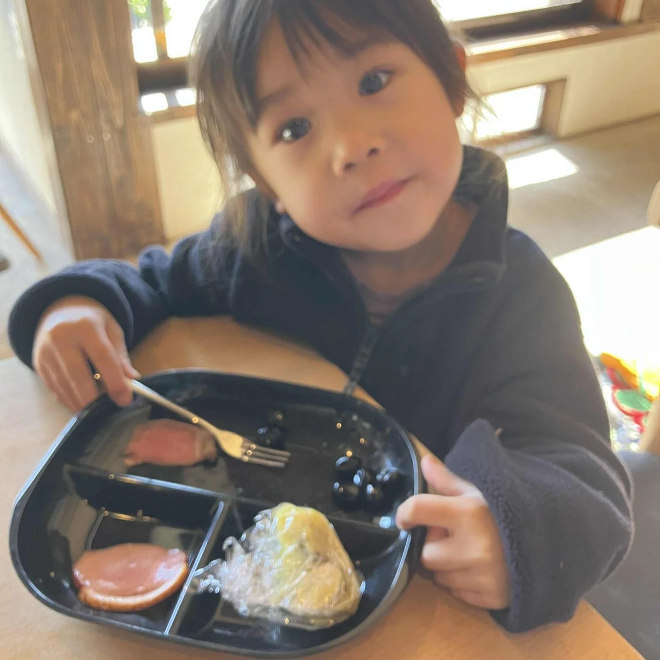 食事が盛り付けられたプレートを持ち、カメラを見つめる幼い子供のポートレート写真です