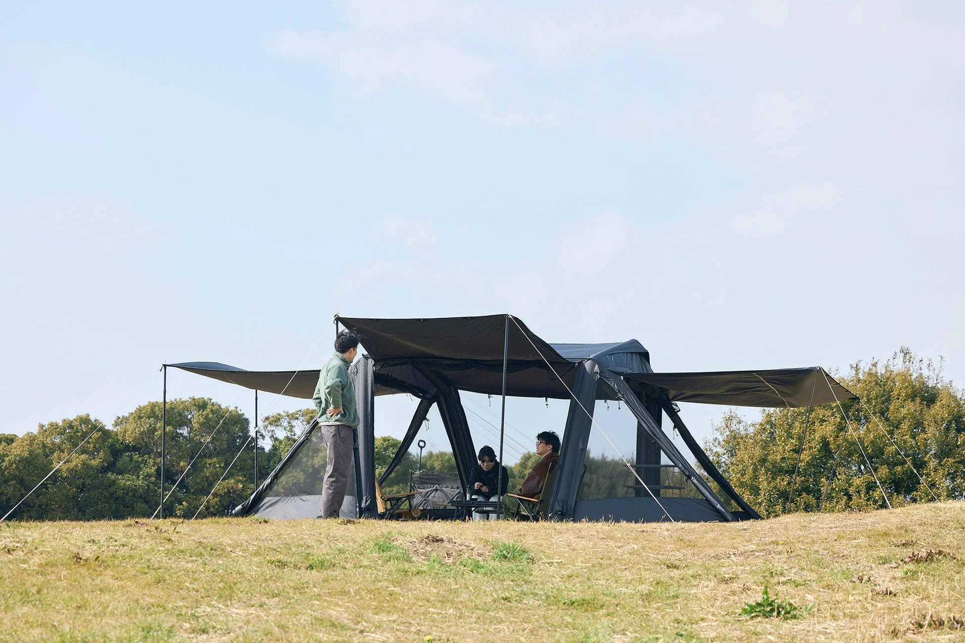 青空の下、広々とした草地で友人たちがキャンプを楽しんでいる様子