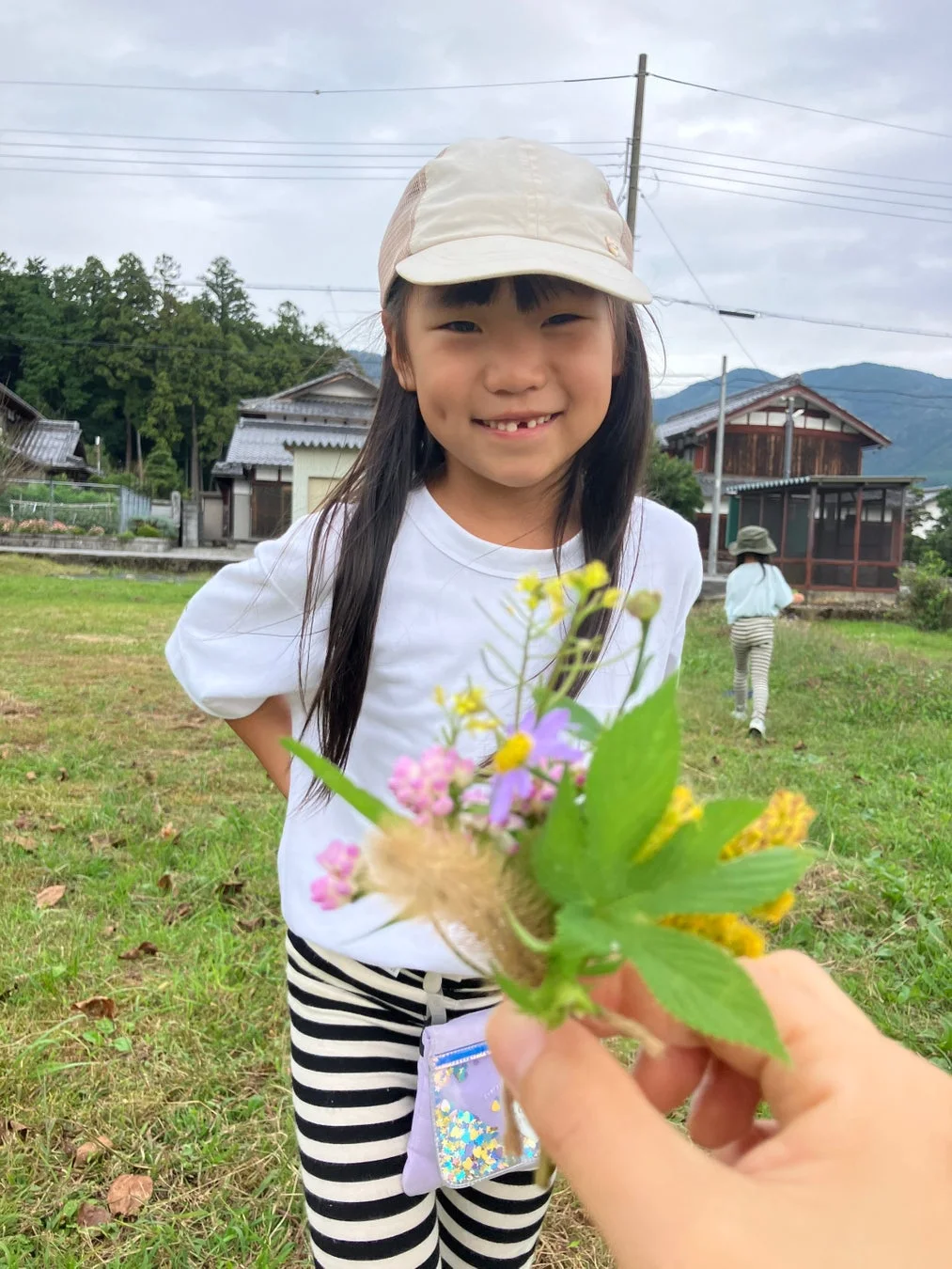 屋外で小さな野花の花束を見つめ、笑顔を向けている子供の姿