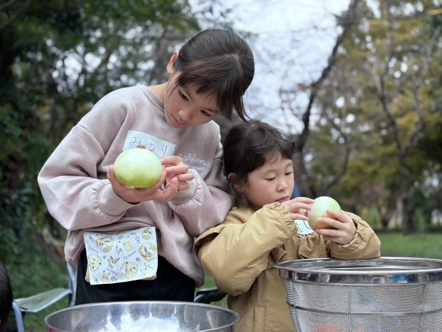 屋外で2人の女の子が玉ねぎを手に持ち、調理の下準備をしているようです