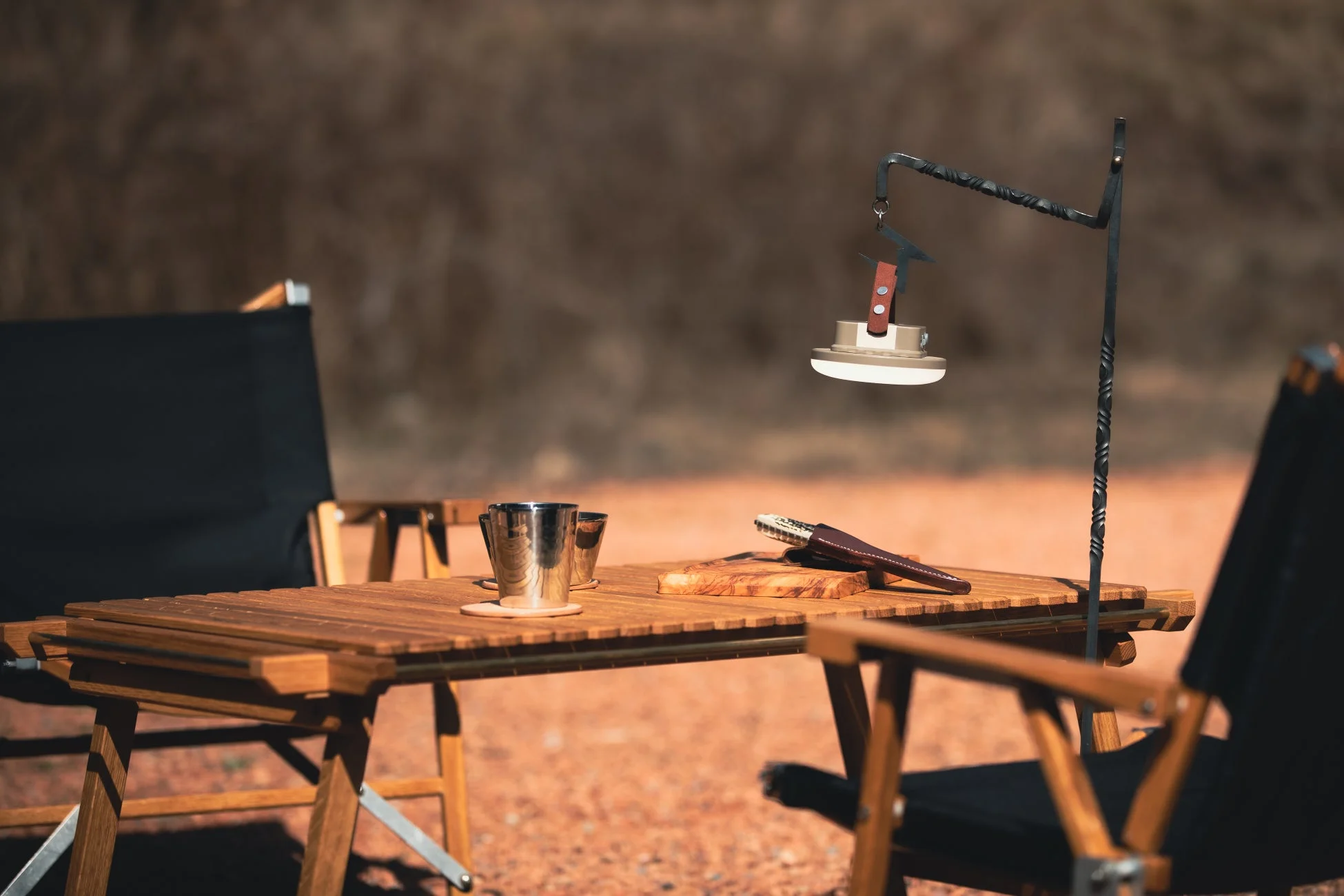 木製のキャンプテーブルと椅子が並べられ、ランタンや食器が置かれたアウトドアの風景