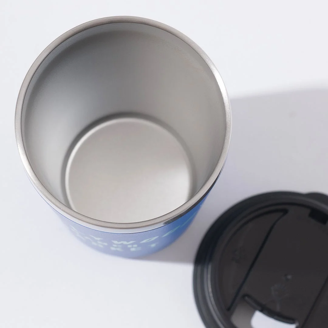 青い保温タンブラーを上から見た写真です。内部はステンレス製で空の状態です。隣には黒い蓋が置かれており、白い背景で撮影されています。