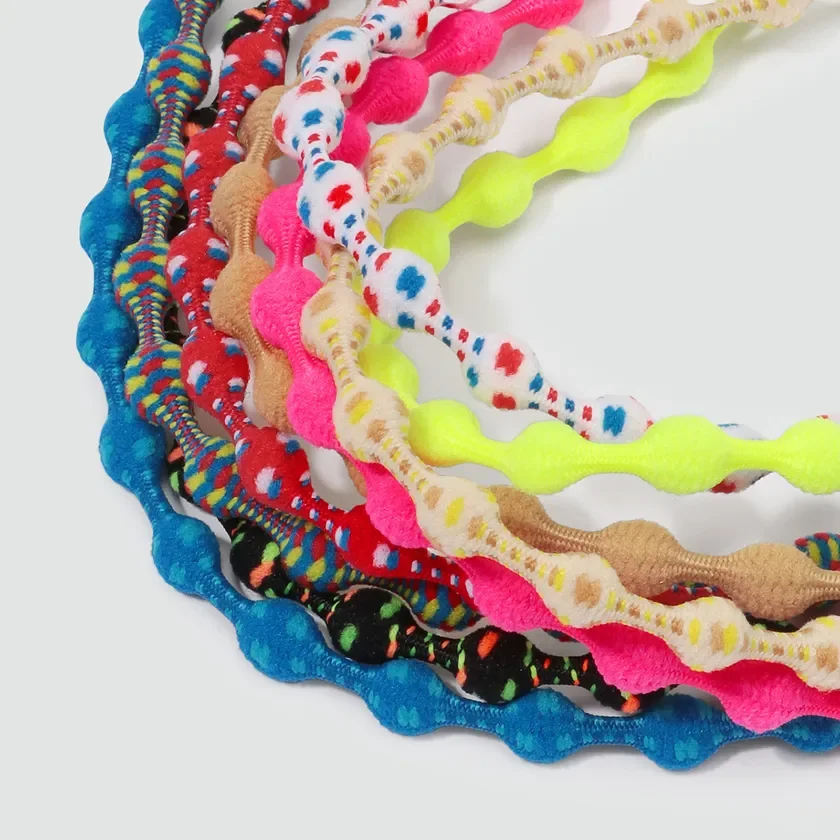 白い背景に、様々な色と模様の波型で凹凸のあるヘアゴムが複数、円形に並べられている様子を捉えた画像です。鮮やかな色が目を引く、ファッショナブルな小物です。