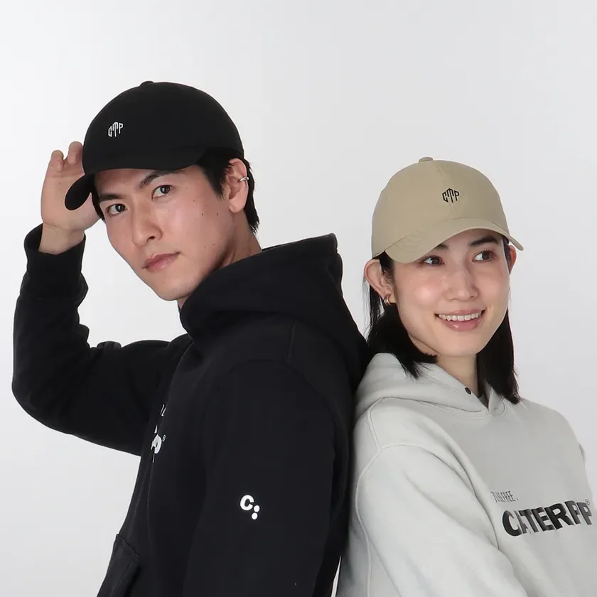 男女2人がカジュアルなフーディーとキャップを着用し、背中合わせに立っている画像です。男性は黒、女性はベージュ系の服を着用しており、ファッションアイテムの紹介に適しています。