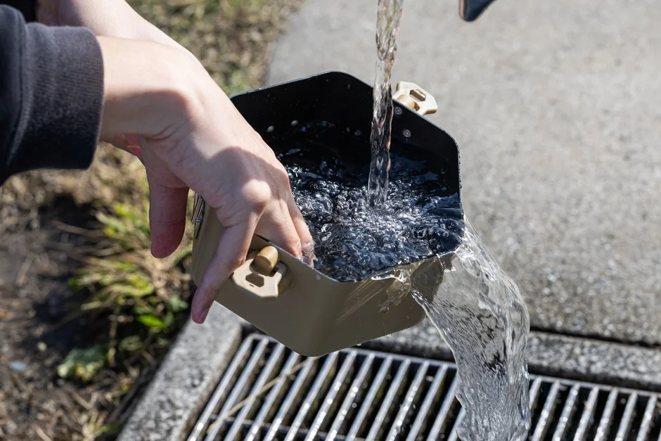 屋外で、人がメスティンのような容器に水を注いでいる様子
