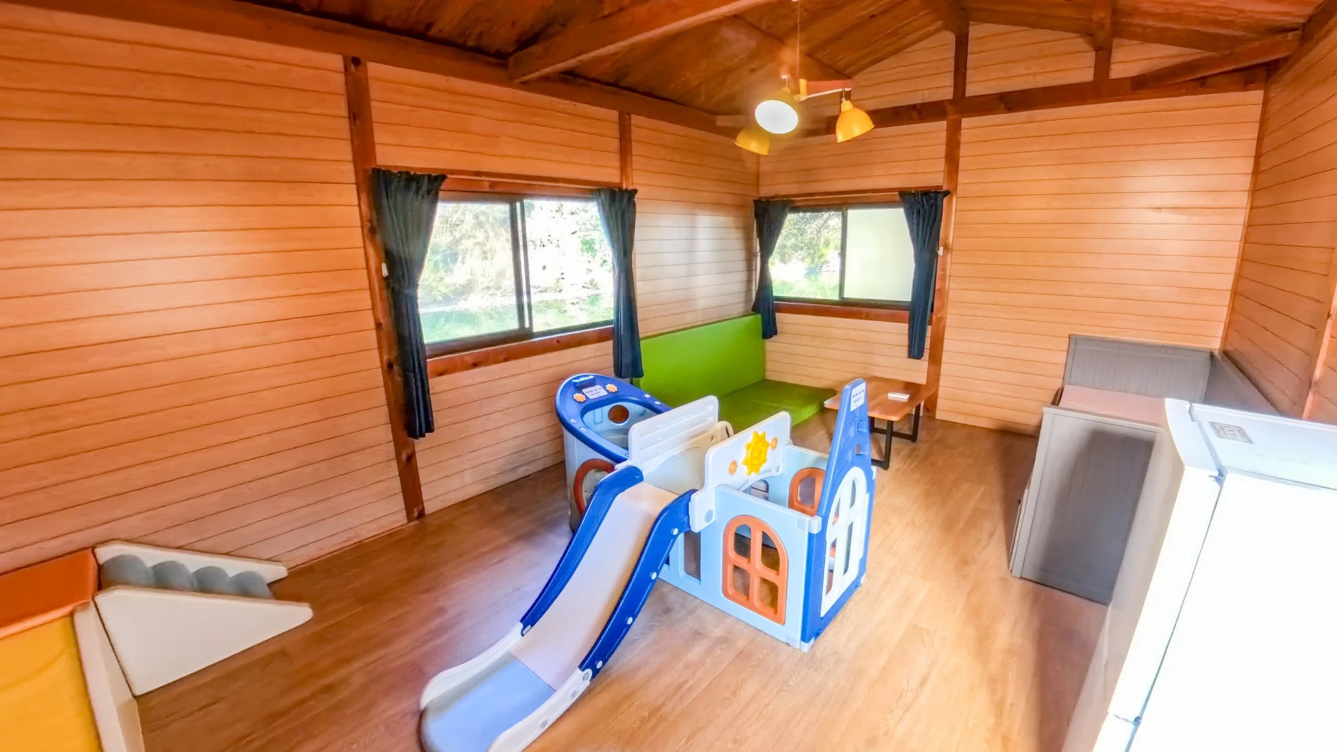木製の壁と天井が特徴的な明るい部屋で、滑り台付き遊具が置かれている