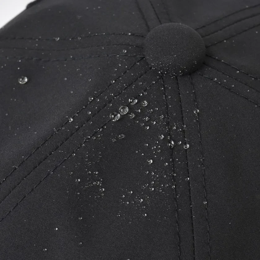 黒い生地の表面に多数の水滴が付着しており、その優れた撥水性を示しています。キャップや帽子の素材の一部をクローズアップした画像です。