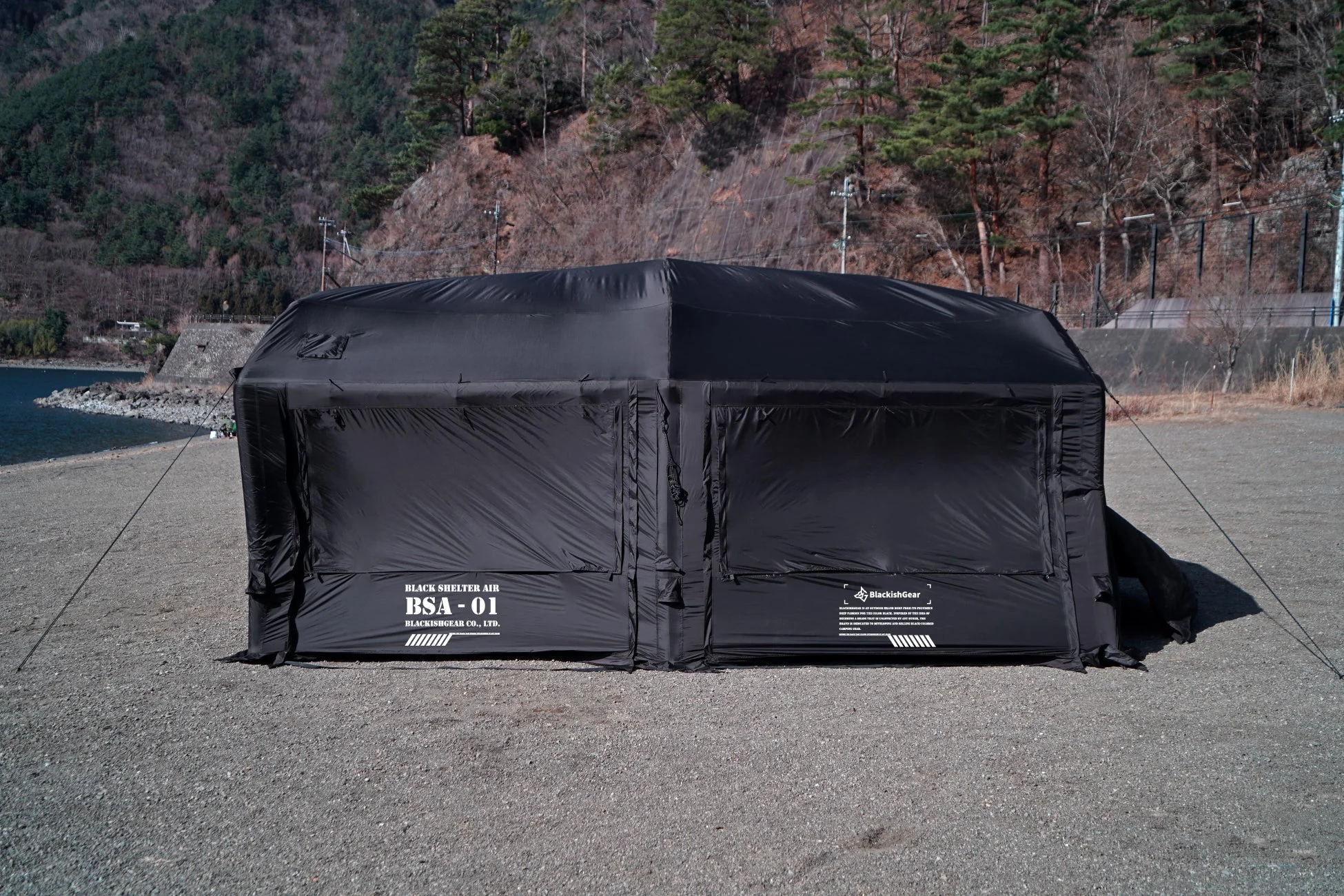 湖畔の砂利地に設置された黒い大型シェルター