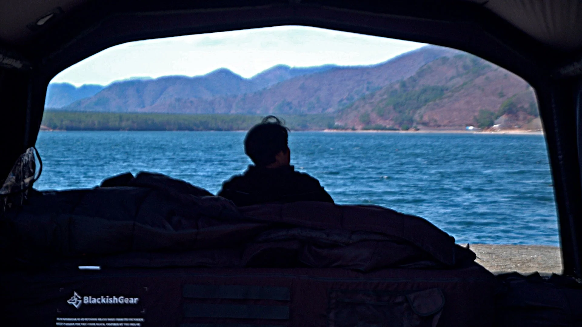 テントの中から湖と山々の景色を眺める人物
