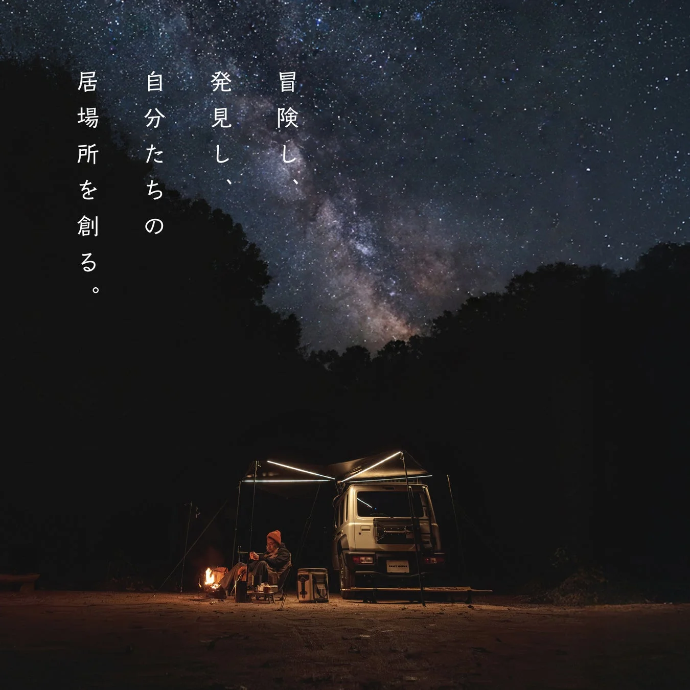 満天の星空と天の川が広がる夜のキャンプ風景。焚き火を囲んでくつろぐ人物と、オーニング付きの車が写っています。