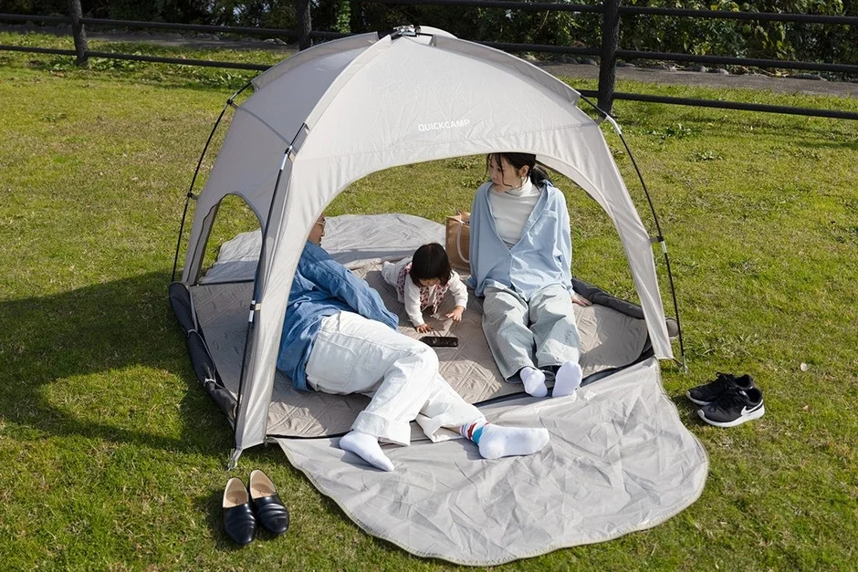 芝生が広がる屋外で、両親と幼い子どもが簡易テントの中でくつろいでいる様子