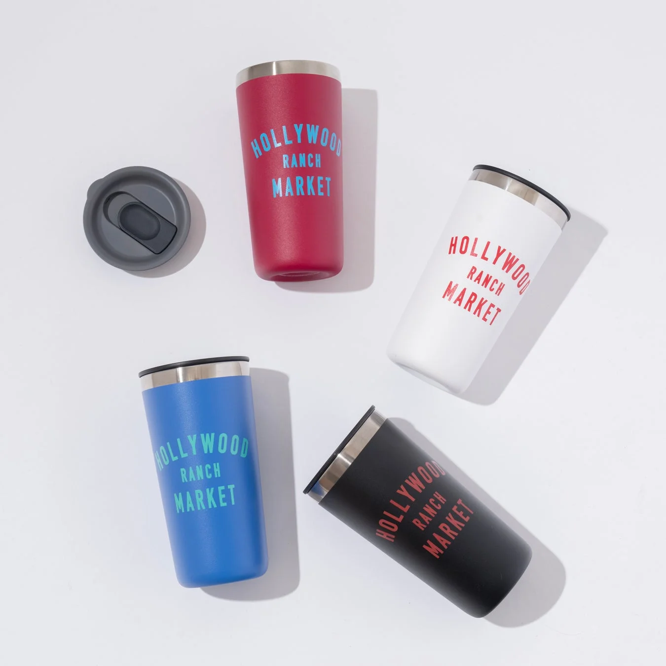 HOLLYWOOD RANCH MARKETのロゴが入ったカラフルなタンブラー5点が白い背景に置かれています。赤、白、青、黒のタンブラーと、外された蓋が一つ写っています。