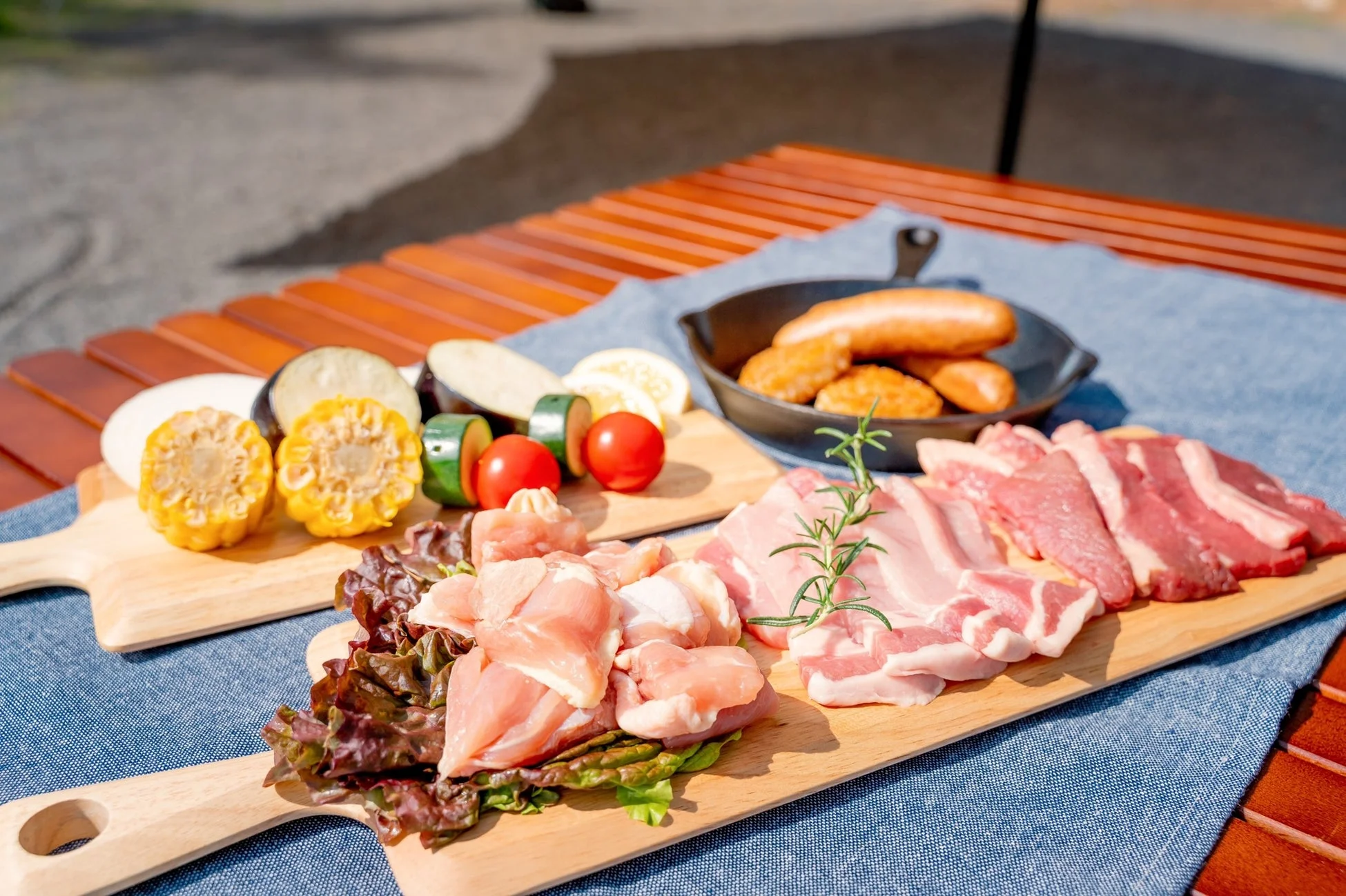 屋外のテーブルに、バーベキュー用の新鮮な肉と野菜が美しく並べられています