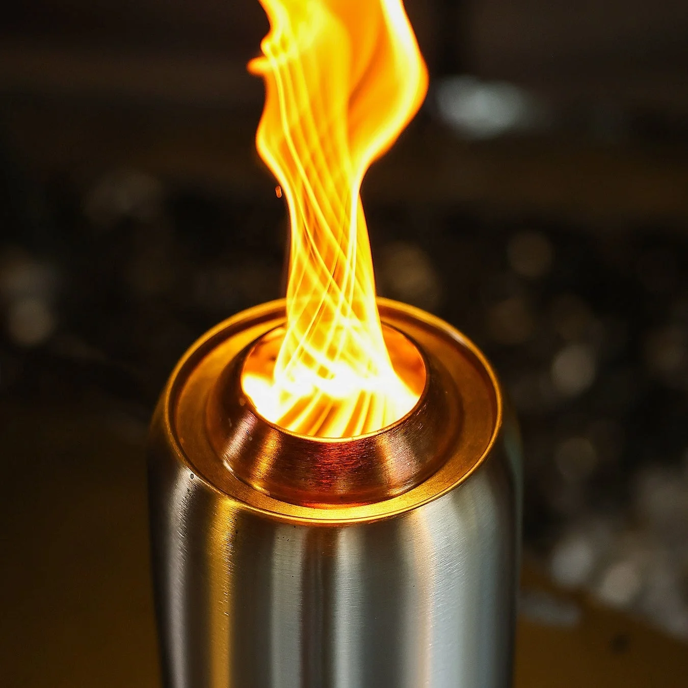 金属製の容器から、明るくオレンジ色の炎がらせん状に立ち上っている様子