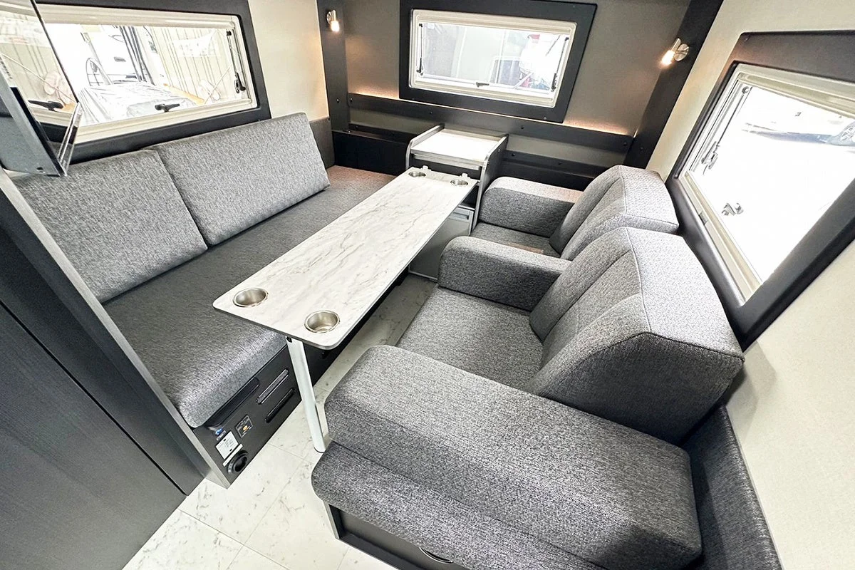 キャンピングカーのモダンな車内リビング空間。グレーのソファと大理石調のテーブルが配置され、窓から光が差し込む快適なダイネットエリア