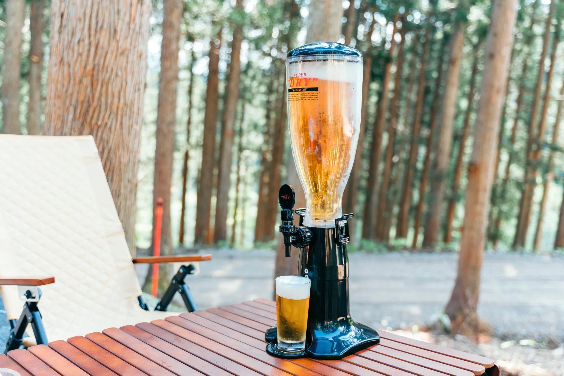 森林を背景に、木製のテーブルに置かれたビールサーバーとグラスのビール