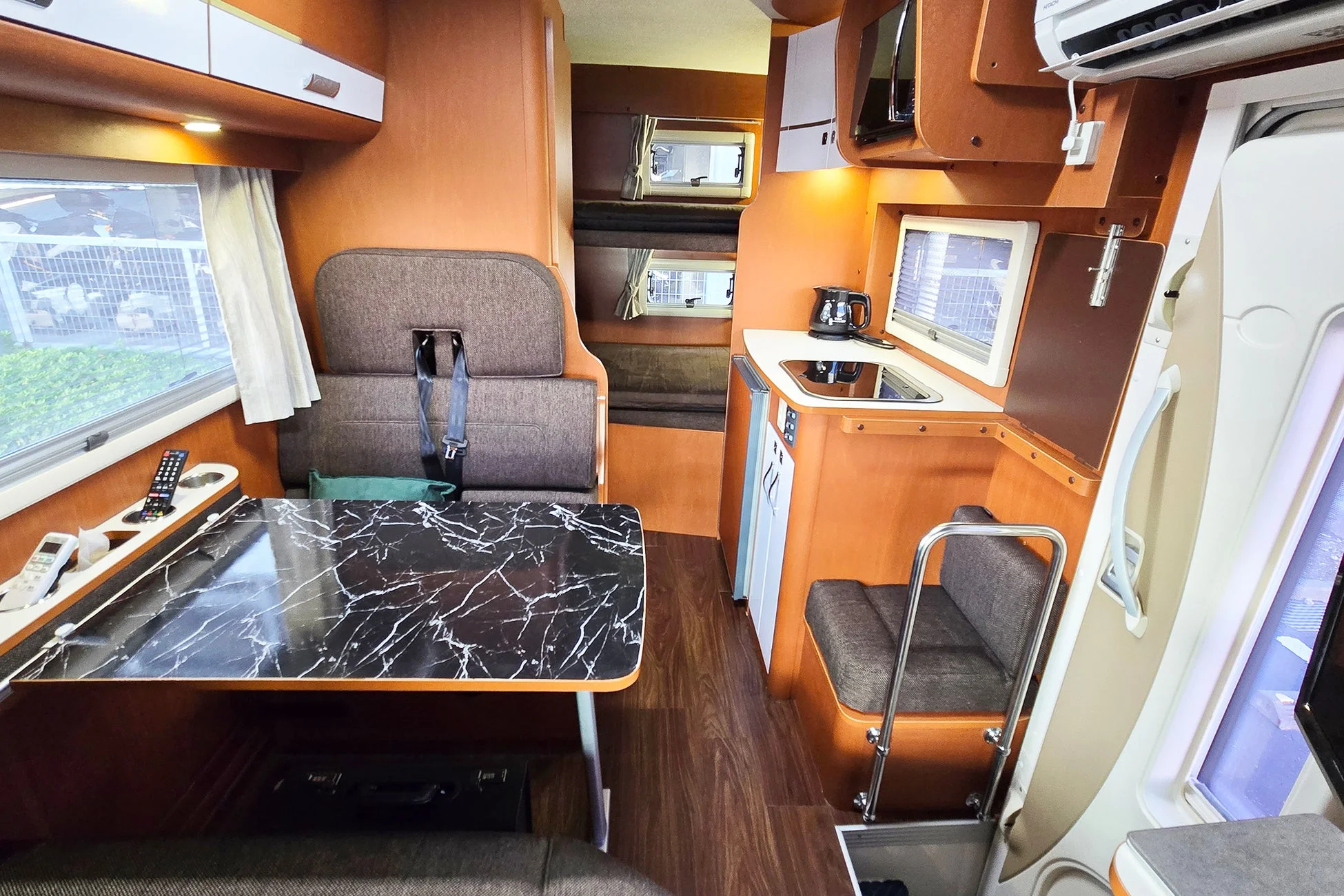 キャンピングカーの快適な車内空間。木目調のインテリアに、ダイニングエリア、簡易キッチン、そして二段ベッドが備え付けられている