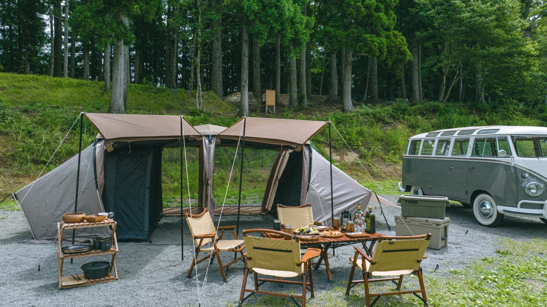森に囲まれたキャンプサイトで、大型テントとヴィンテージのフォルクスワーゲンバス