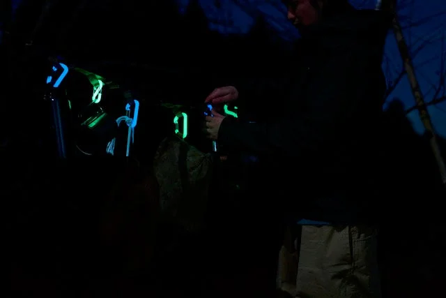 暗闇の中で、青や緑に光る複数のカラビナを操作する人物が写っています