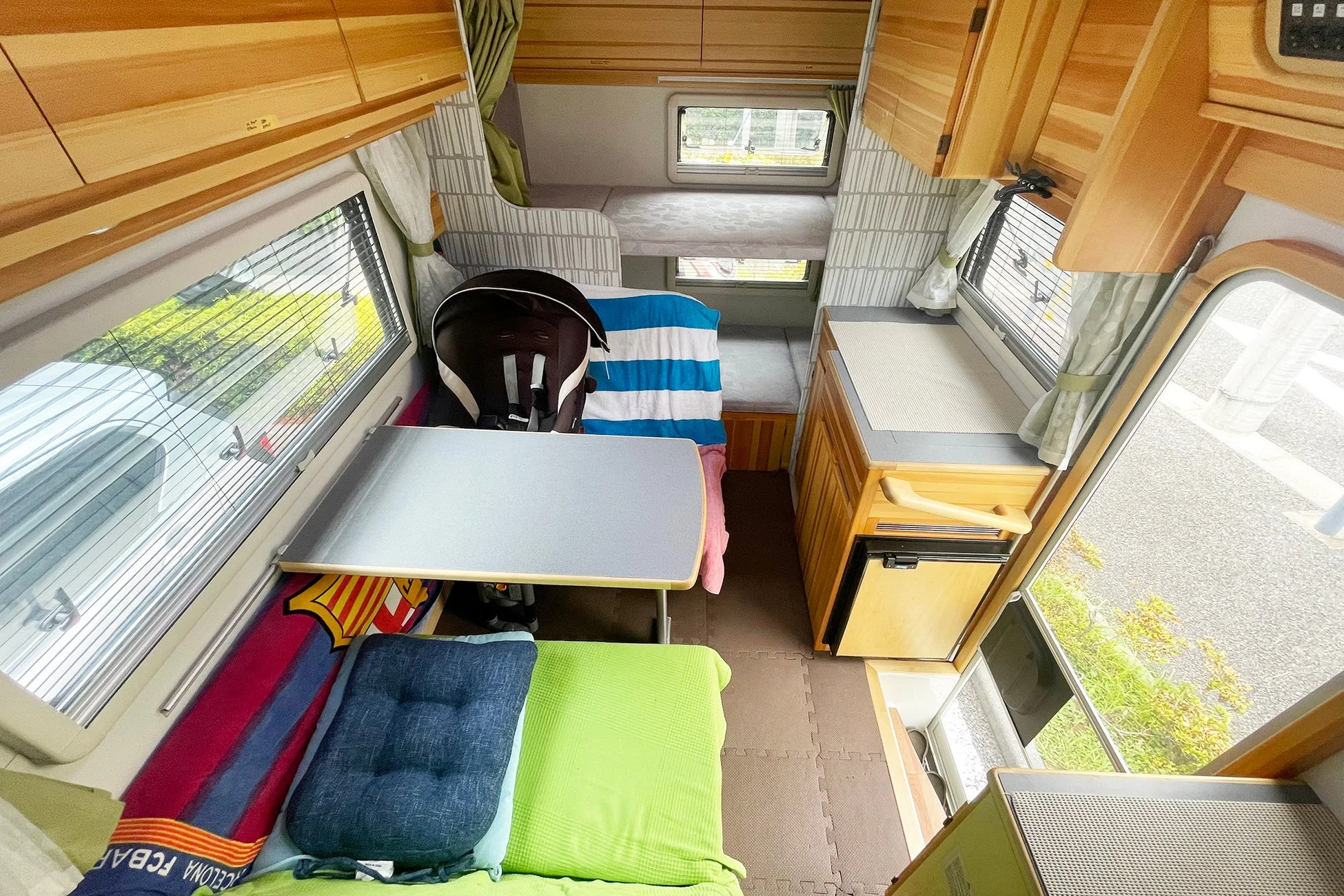 キャンピングカーの機能的な車内風景。木目調の家具で統一され、二段ベッド、テーブル、コンパクトなキッチンエリアが見える