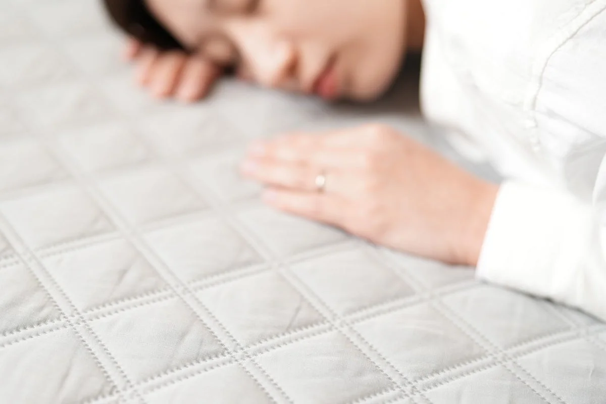 キルティング加工された白い寝具に横たわり、静かに休息をとる女性の姿