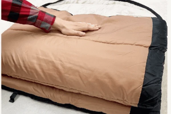 たたまれた茶色い寝袋の表面を手のひらで押している様子