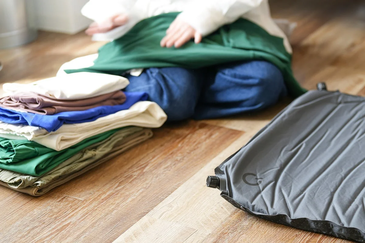 フローリングに衣類とエアマットが置かれ、畳む人物