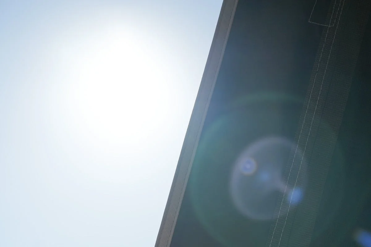 明るい太陽光が画面左上から差し込み、強いレンズフレアが印象的な一枚。画面の右側には暗い構造物の一部が斜めに写り込んでおり、抽象的な雰囲気を作り出しています。