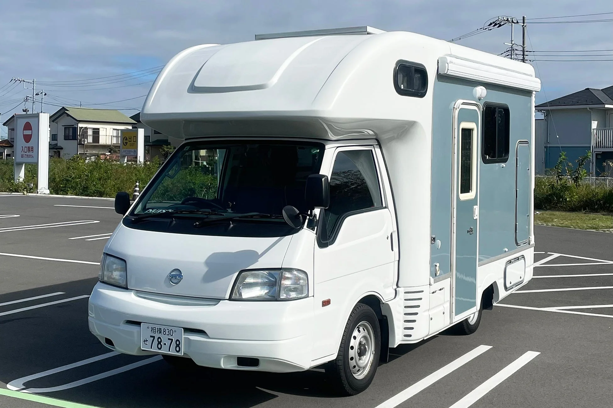 晴れた日に駐車場に停められた、白と水色のモダンなキャンピングカーの正面からの写真