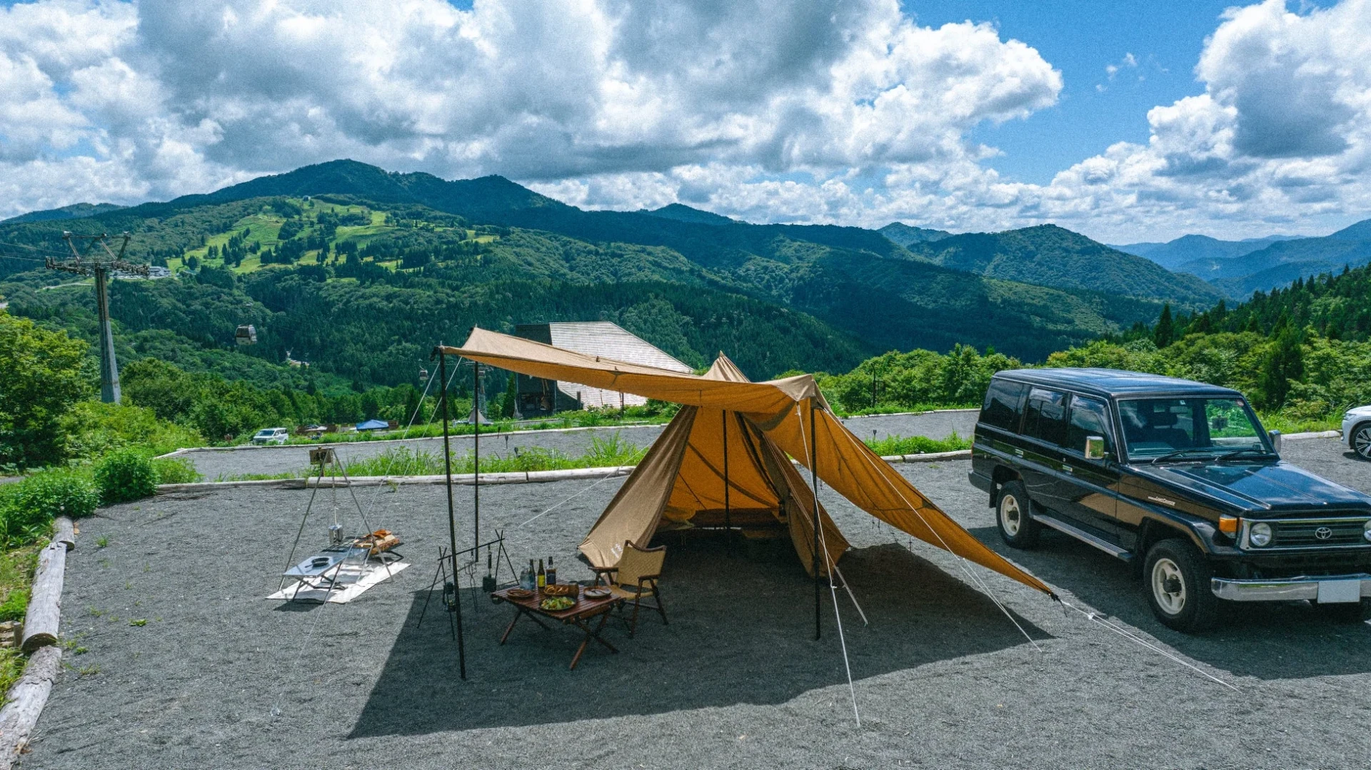広大な山々を背景にキャンプサイトに設営されたテントとタープ、そして黒いランドクルーザー