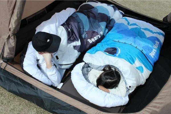テントの中で大人と子供が寝袋に入ってリラックスしている様子