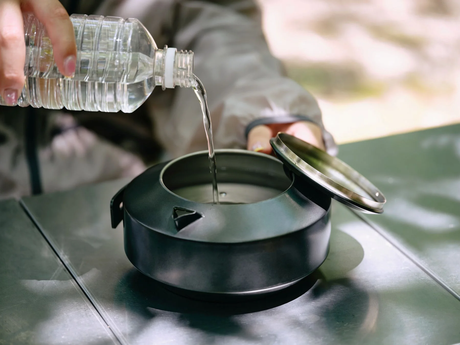 屋外で透明なペットボトルから黒いケトルに水を注ぐ様子