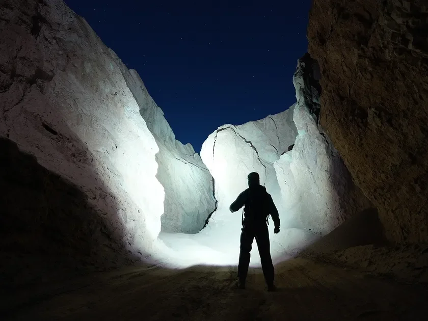 暗い夜の峡谷で懐中電灯の光を前方に向けた人物