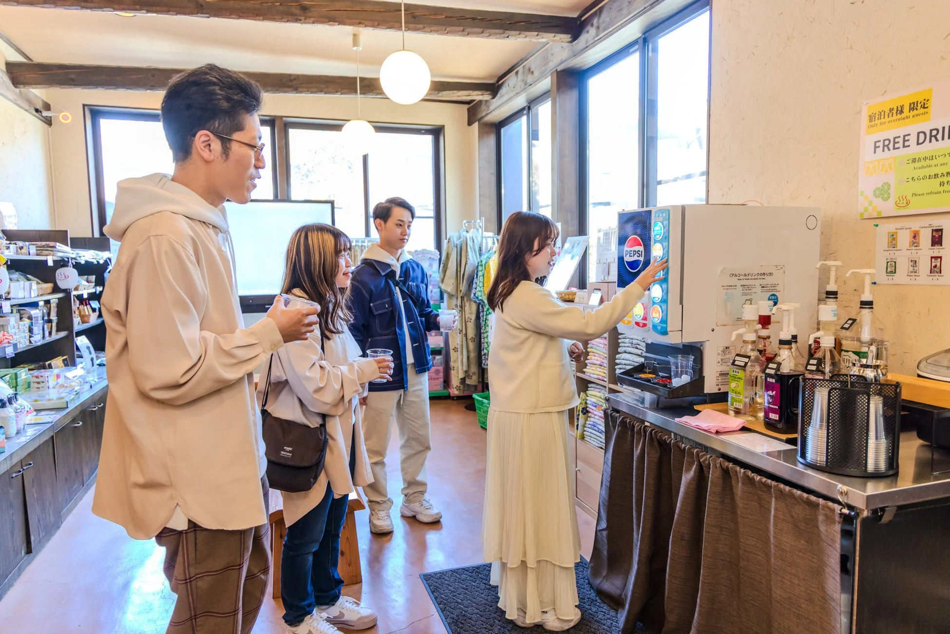 宿泊施設内のフリードリンクコーナーで、若者たちが飲み物を選んでいる様子。ペプシのドリンクバーがあり、宿泊者限定で利用できるサービス。アルコールシロップなども用意され、友人同士で会話しながら楽しんでいる。