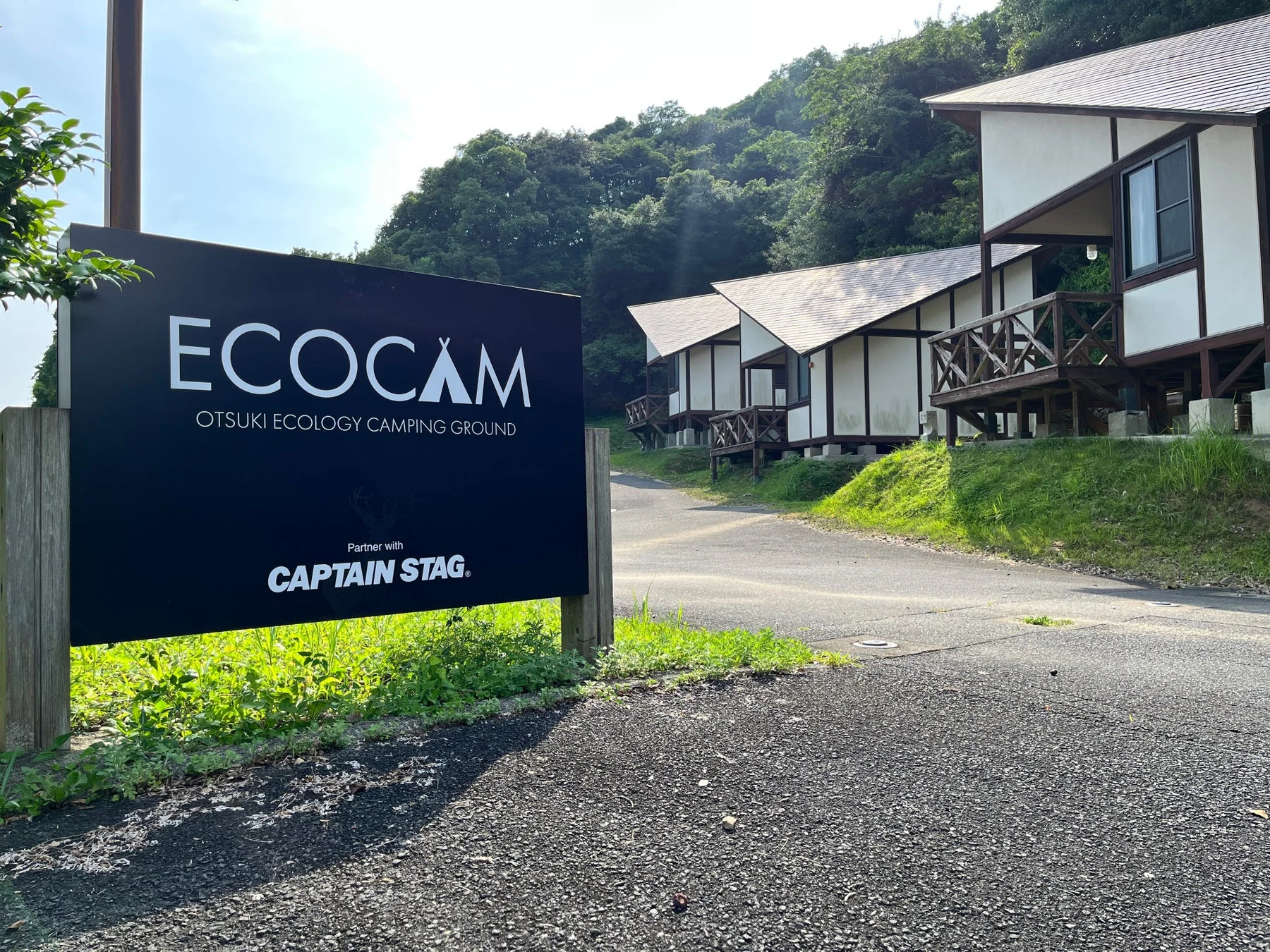 大月エコロジーキャンピンググラウンド「ECOCAM」の看板と、山間の自然に囲まれたモダンな宿泊施設