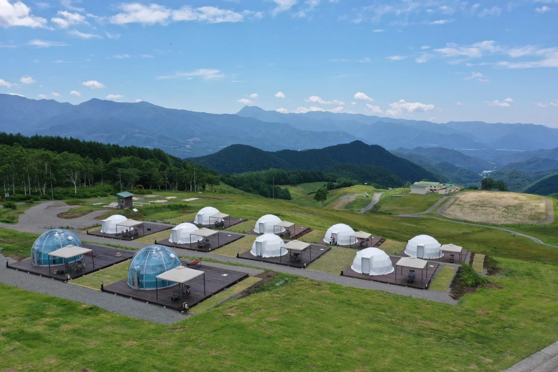山々の壮大な景色を背景に、ドーム型テントが整然と並ぶグランピング施設