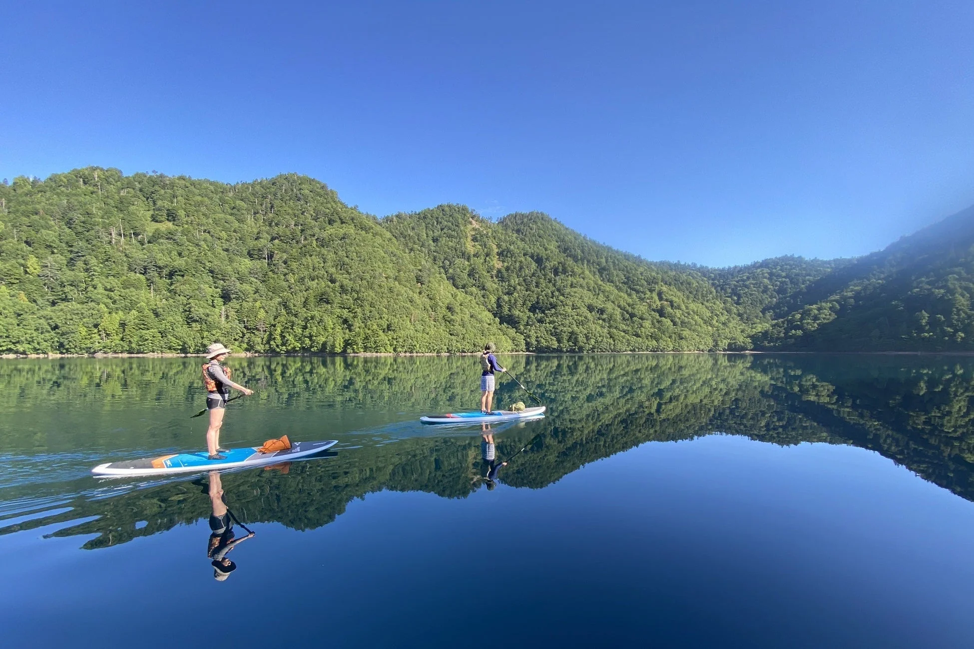 穏やかな湖で二人がSUPを楽しむ夏の風景