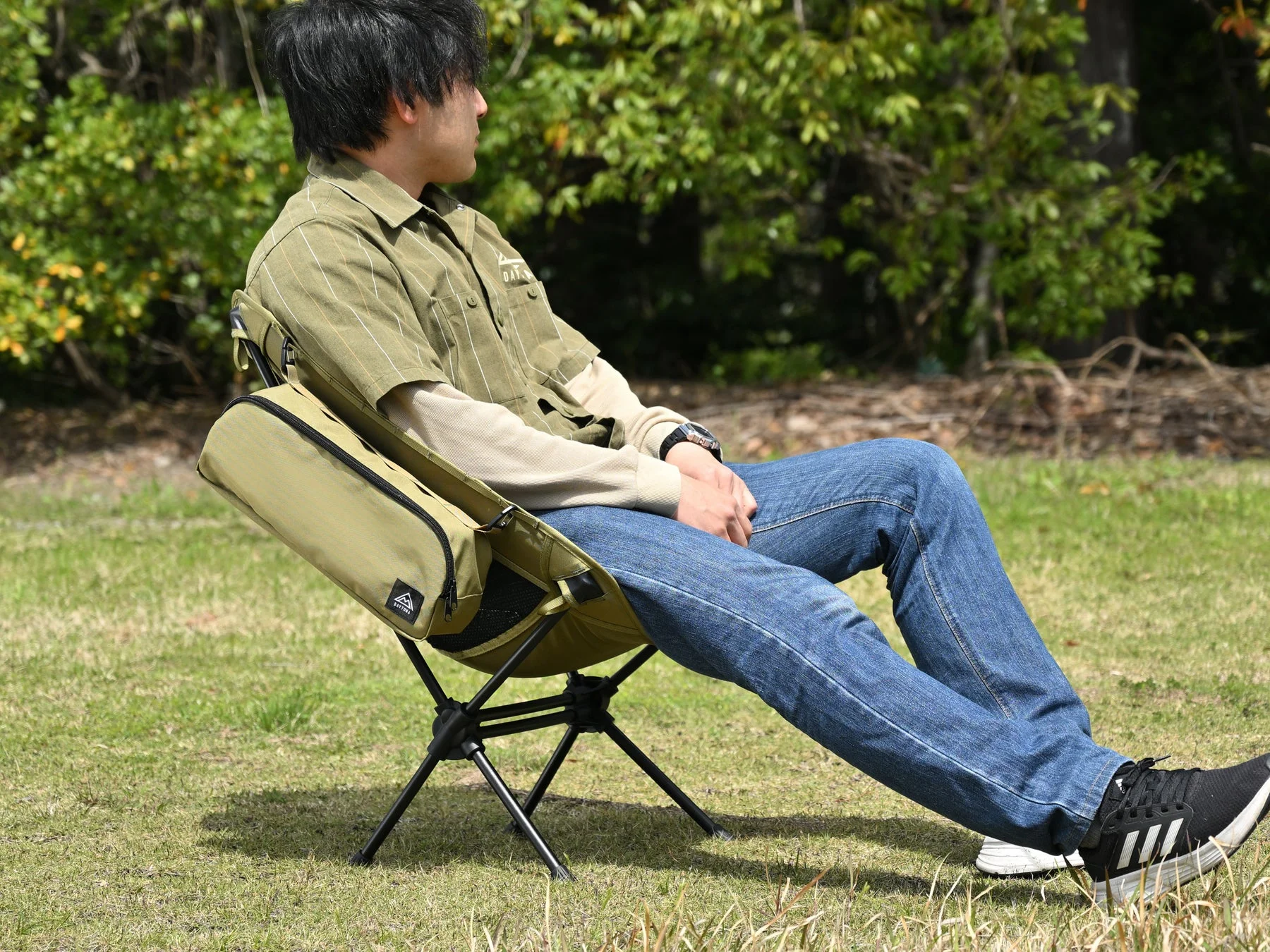 草地の屋外でオリーブ色のポータブルキャンプチェアに座りリラックスしている男性